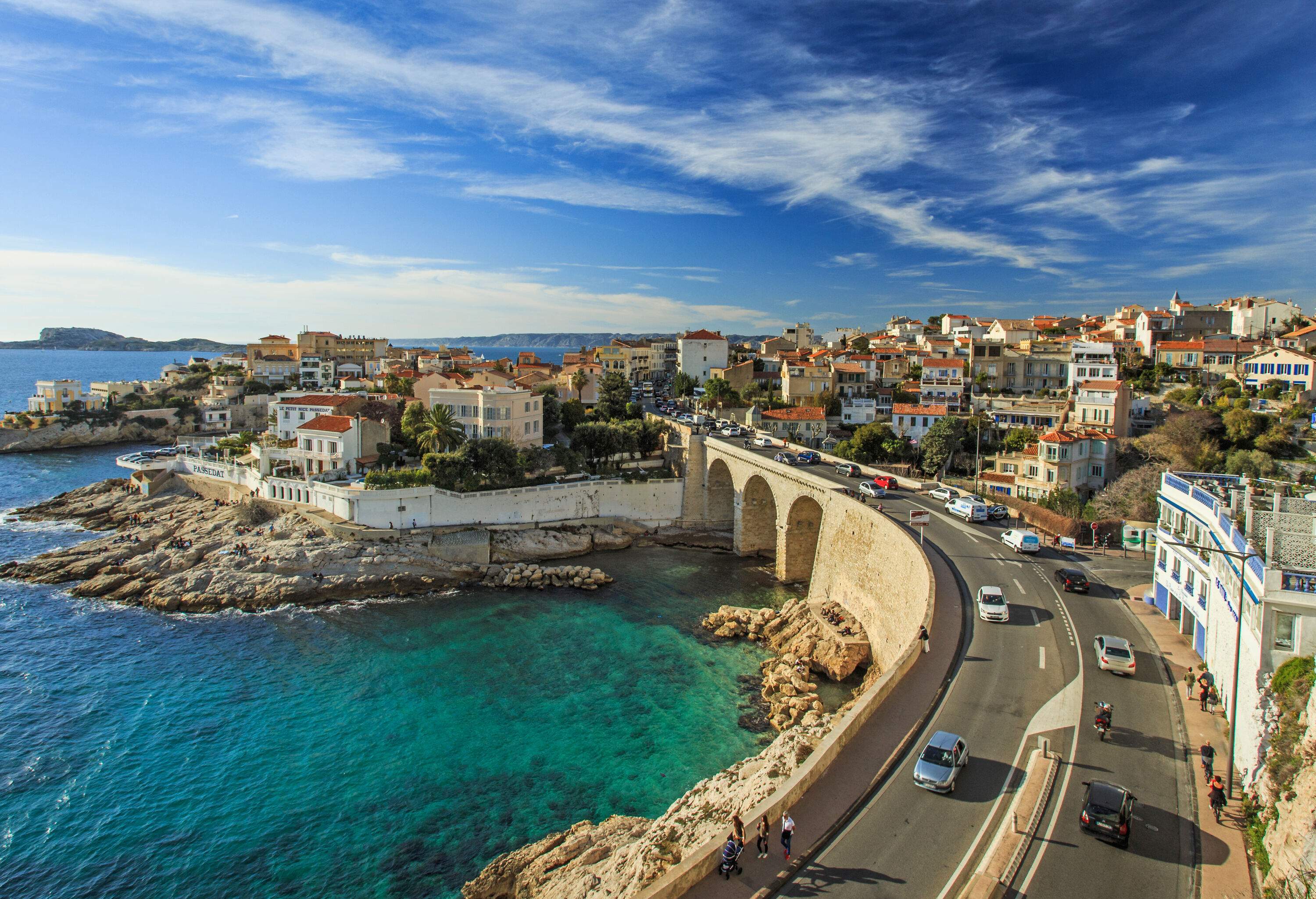 A busy road along a steep and rocky coastline with cityscape views.