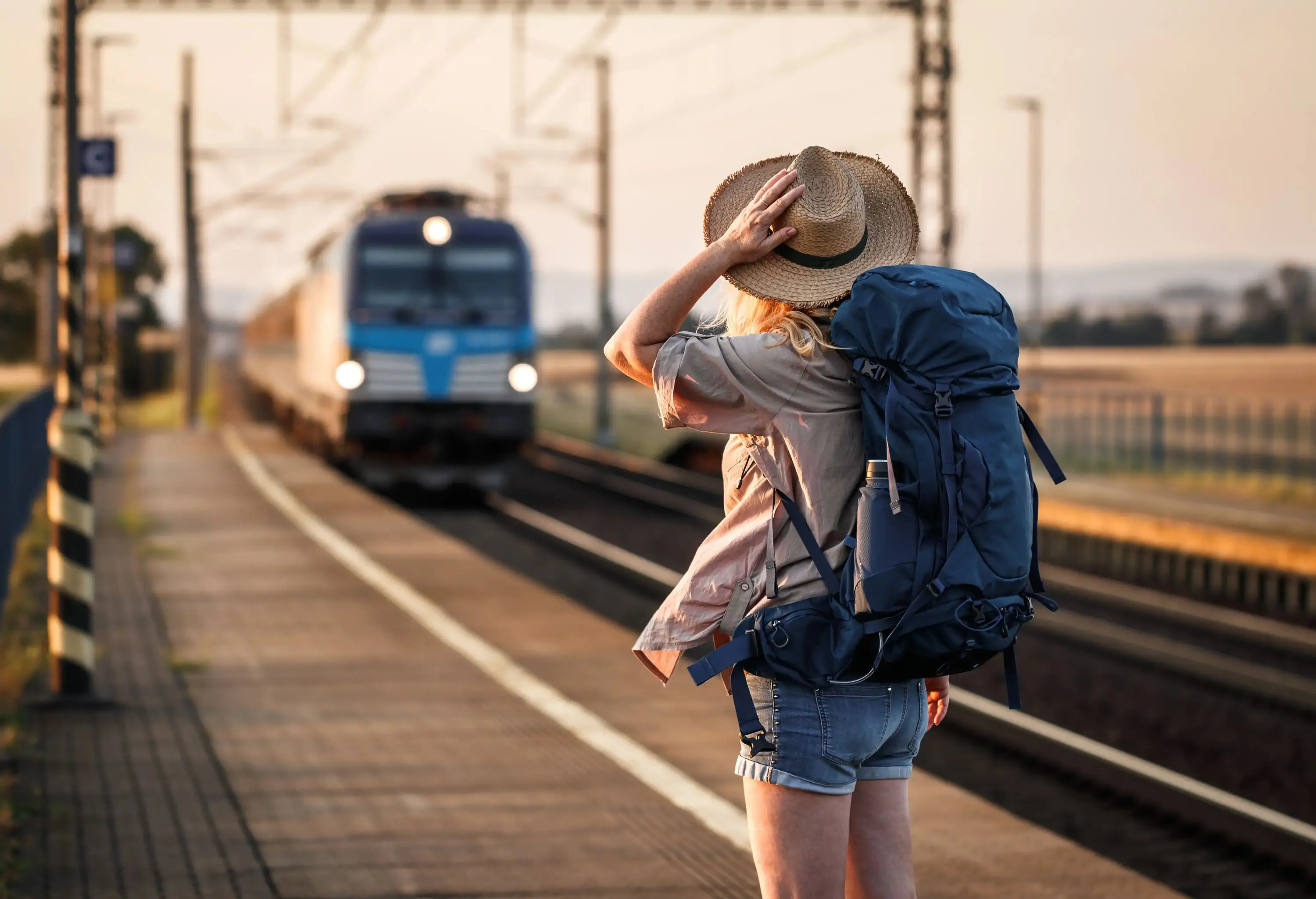 Woman backpacker with hat standing at railroad station and looking to arriving train